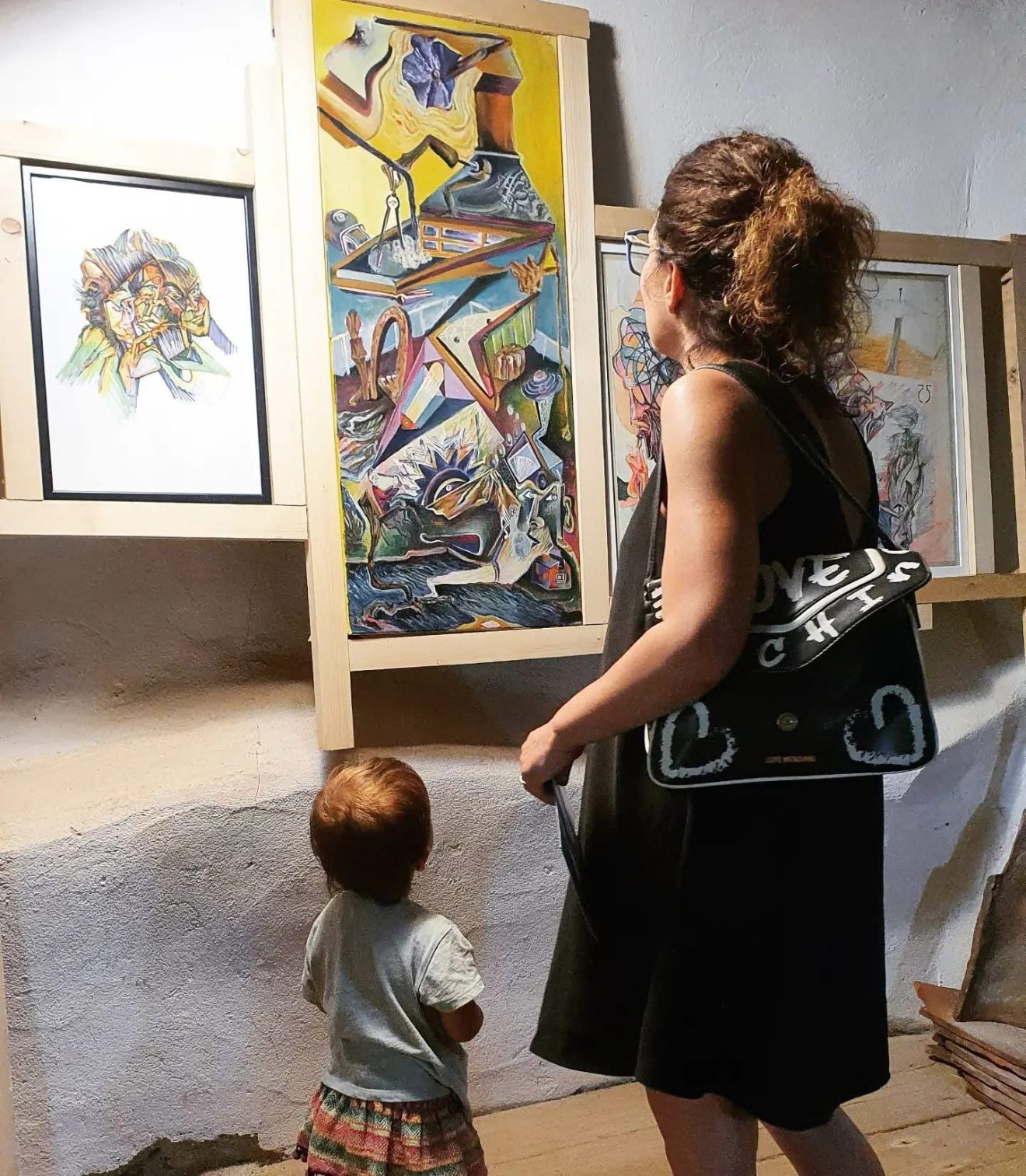 Vizitator și un copil privind picturi de Daniel Gaciu la o expoziție