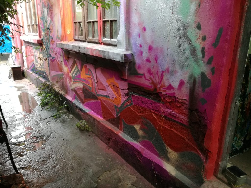 Street art mural in pink and green tones on a building wall
