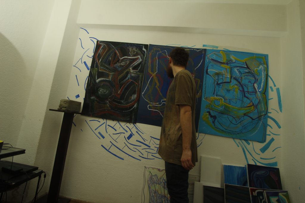The artist standing in front of a large painting on the atelier wall