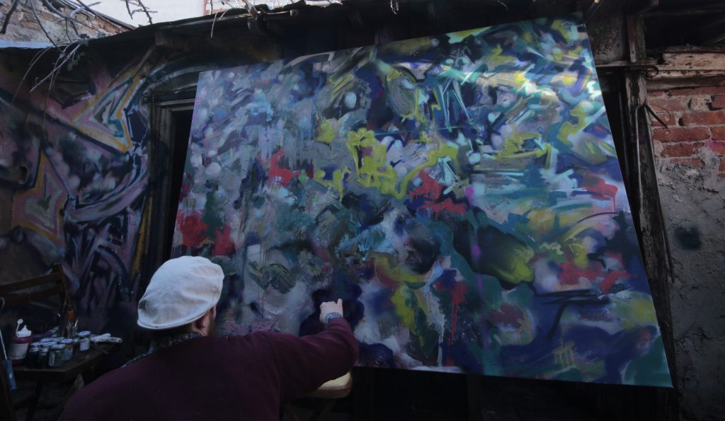 The artist painting a large mural in a workshop space